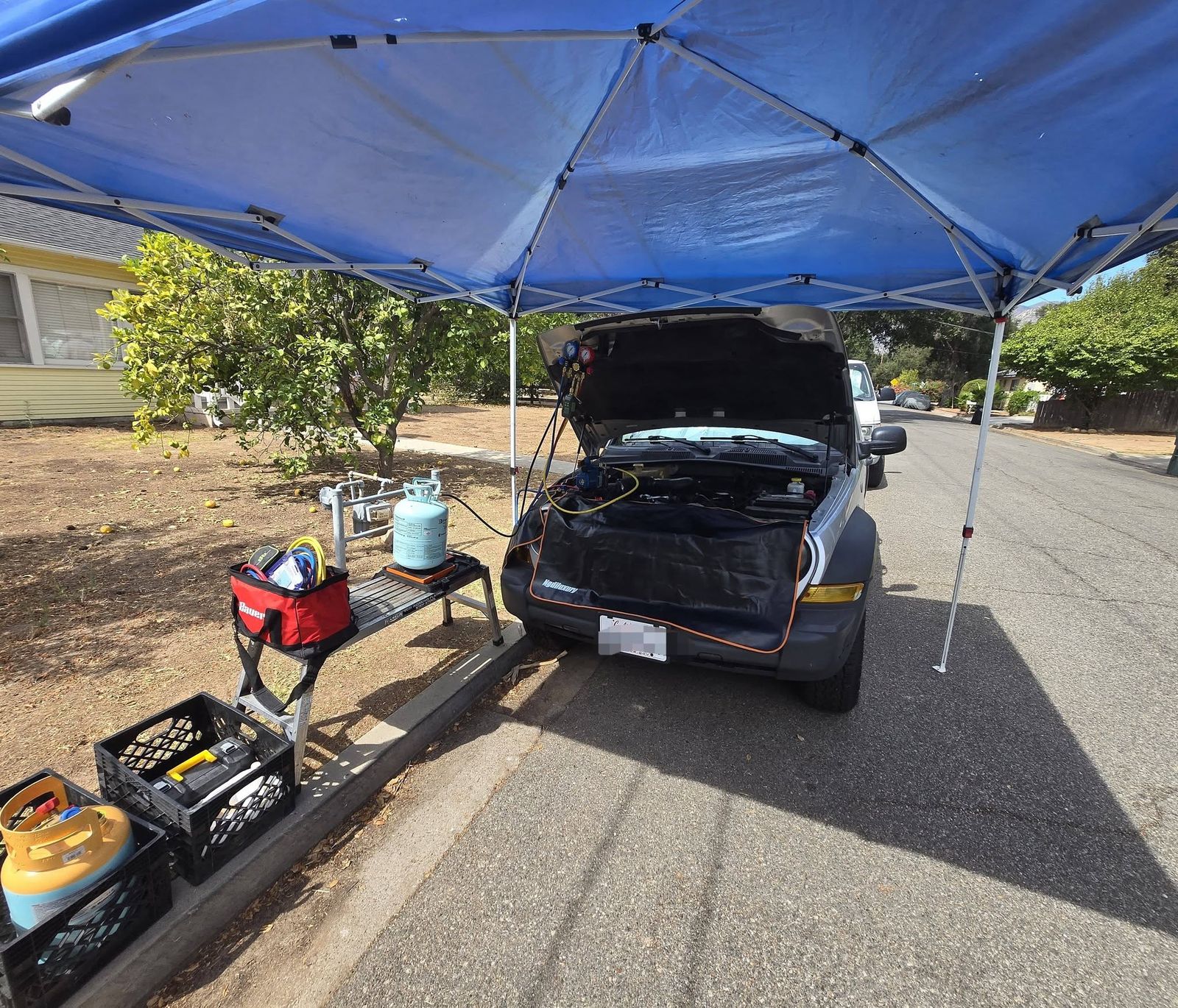 SUV under a blue canopy at the curb with A/C recharge equipment set up beside it