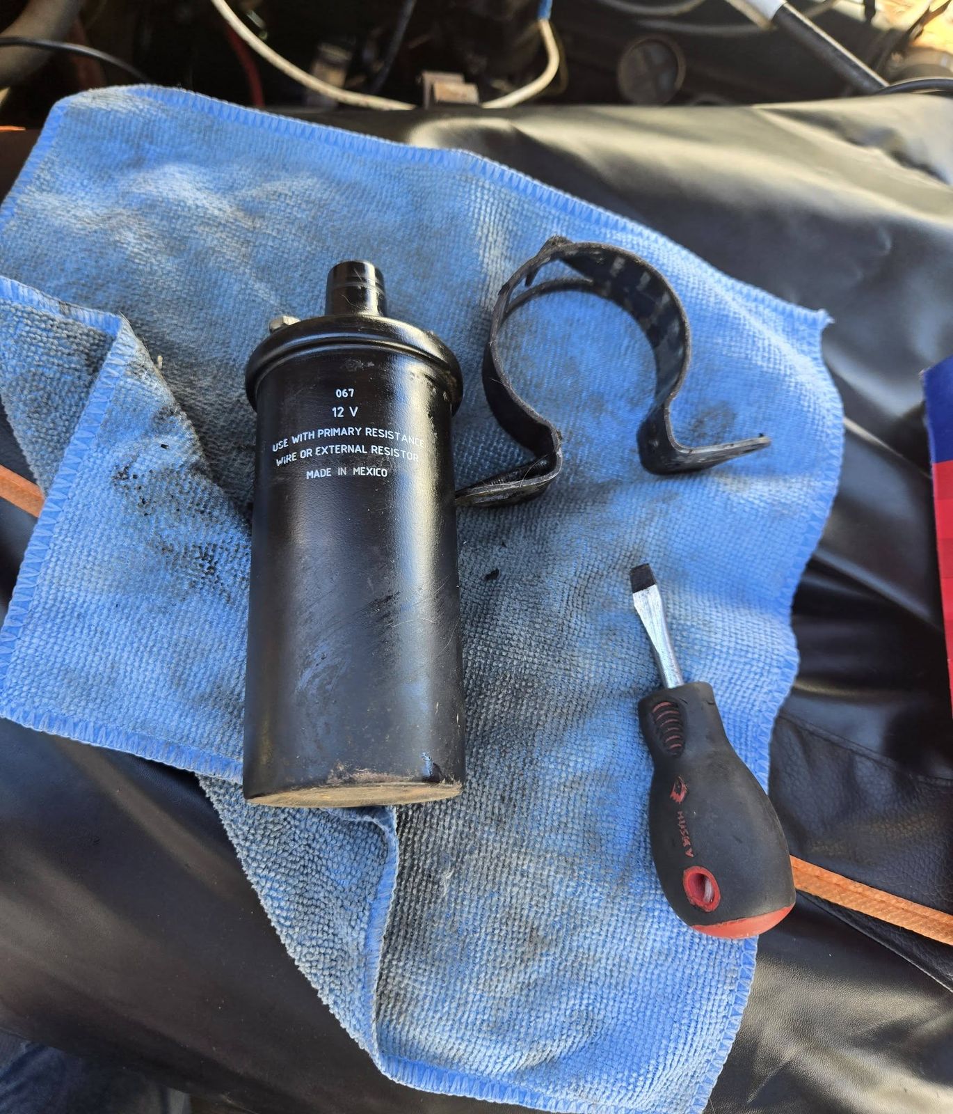 Ignition coil and mounting bracket on a shop towel next to a screwdriver