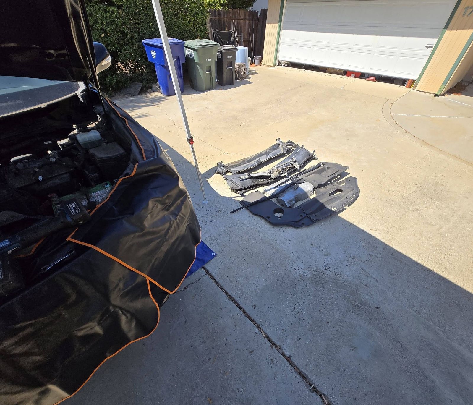 Car with a fender cover on in a driveway, removed trim pieces laid out on the pavement