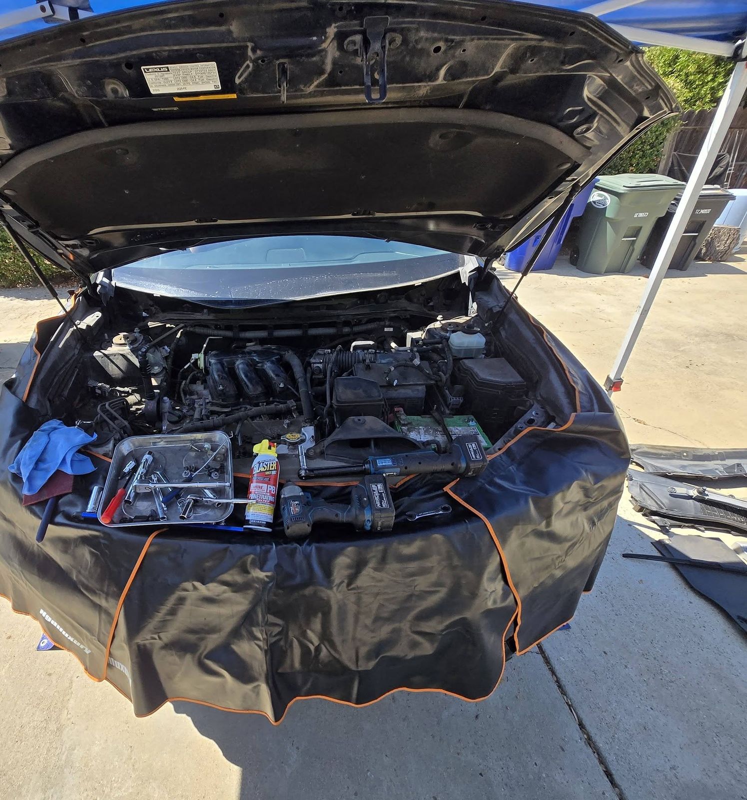 Lexus with the hood up and a fender cover on under a canopy, tools laid out on the engine