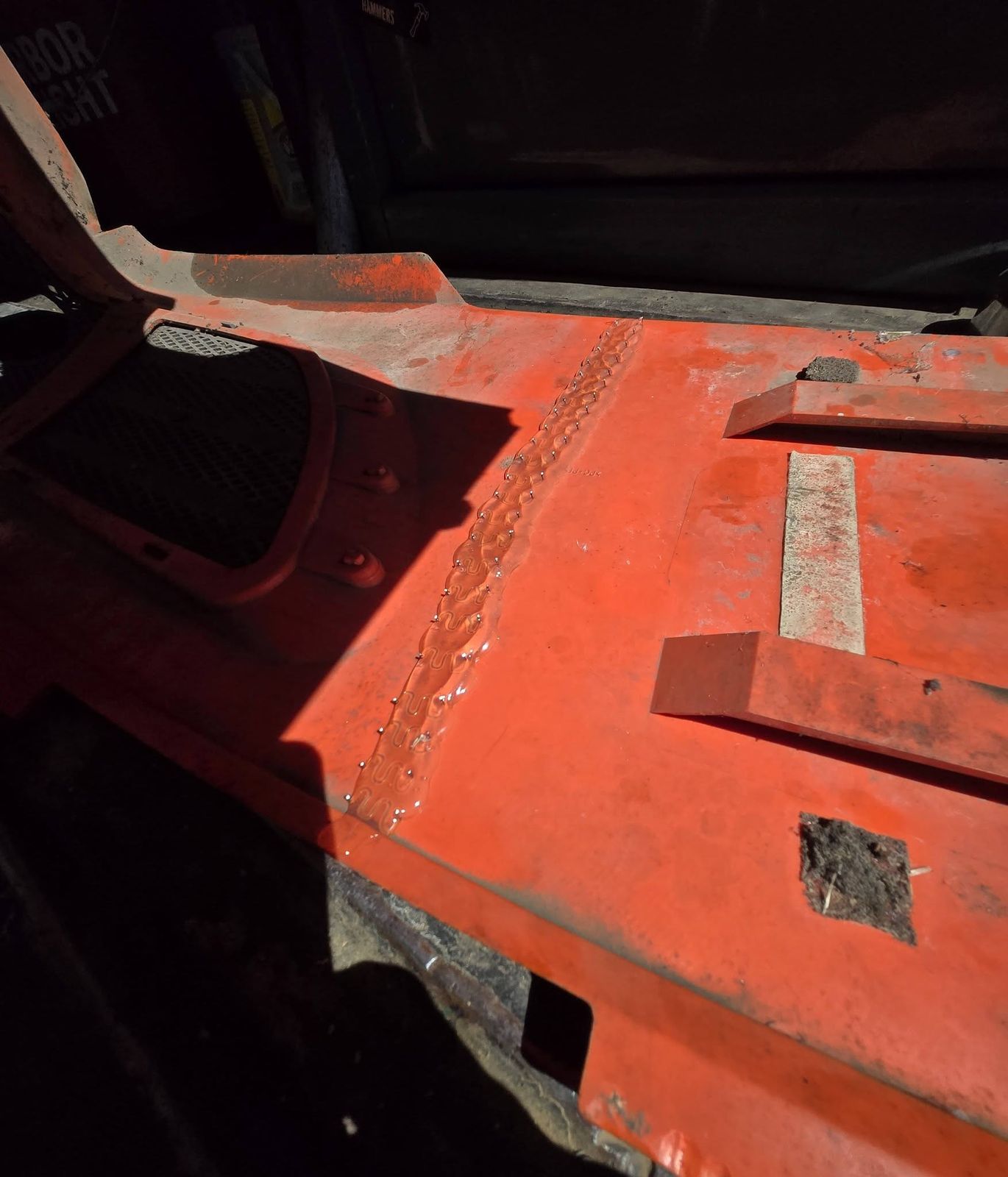 Welded repair on the inside of an orange tractor hood panel